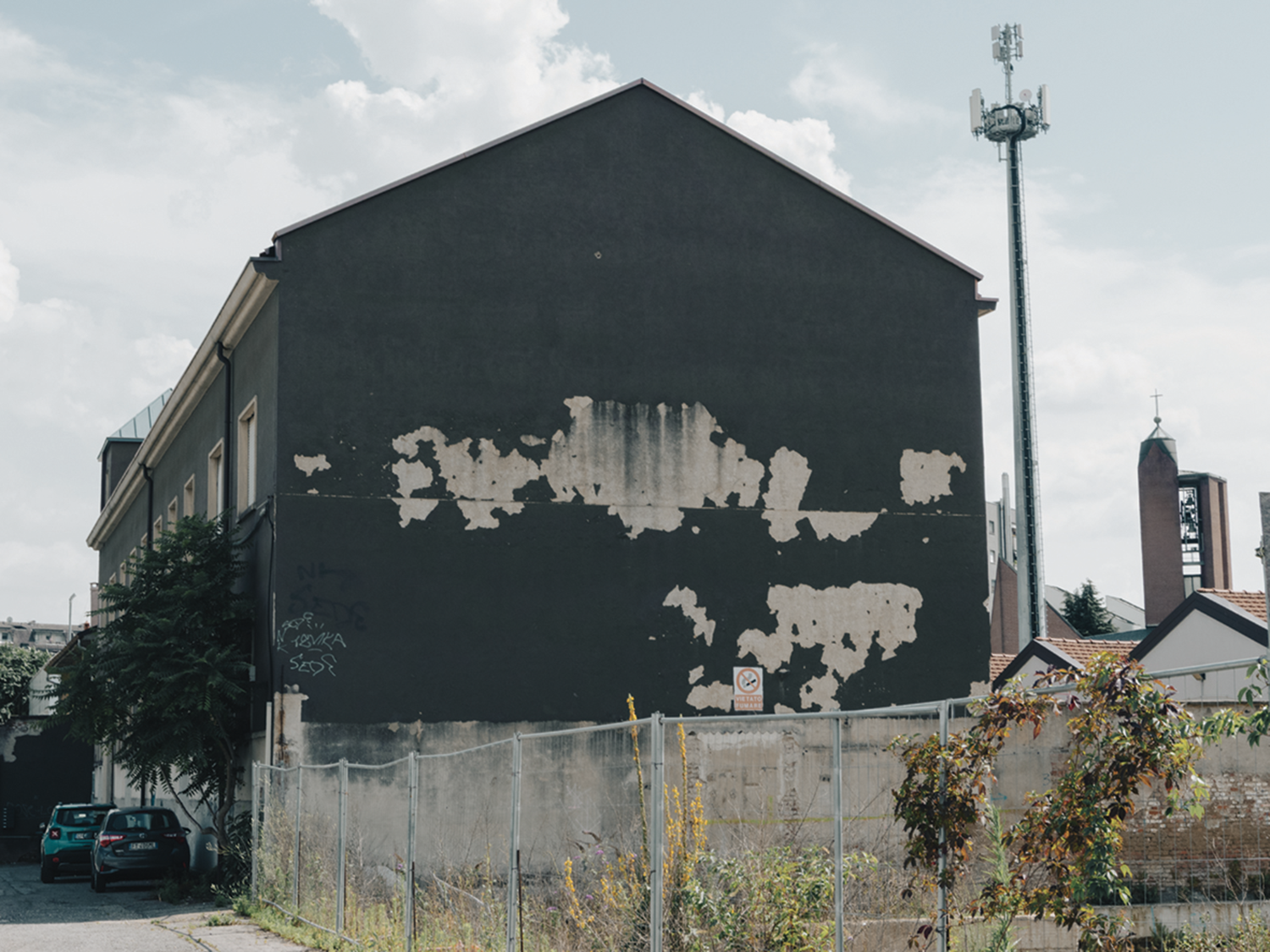 Alt: Mai+ Bologna - Opera dal titolo «1969 - liberamente ispirata» - foto dal vivo dell‘opera: si tratta di un‘incisione in intonaco bianco sul muro di un palazzo il cui intonaco di base è color terra bruciata, e ne compone una parte a mezzaluna sull’angolo del palazzo stesso